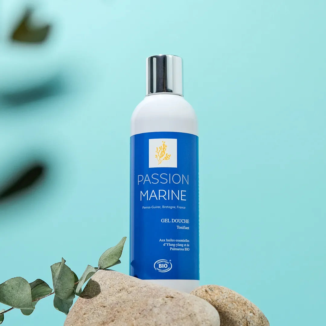 Bouteille de gel douche Passion Marine sur fond bleu avec pierres et feuilles.
