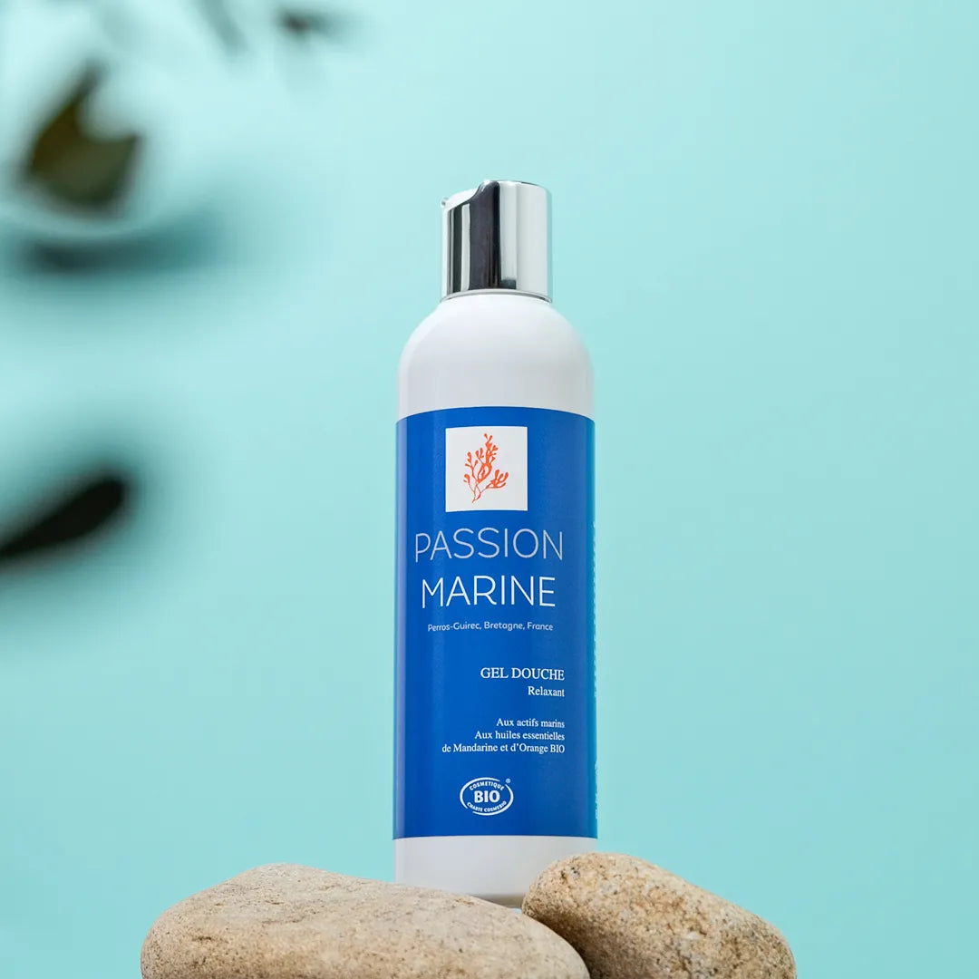 Bouteille de gel douche Passion Marine sur fond bleu avec des pierres.