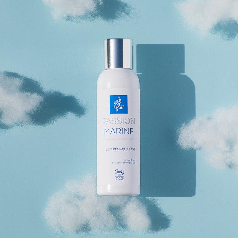 Bouteille de lait démaquillant Passion Marine sur fond bleu avec nuages.