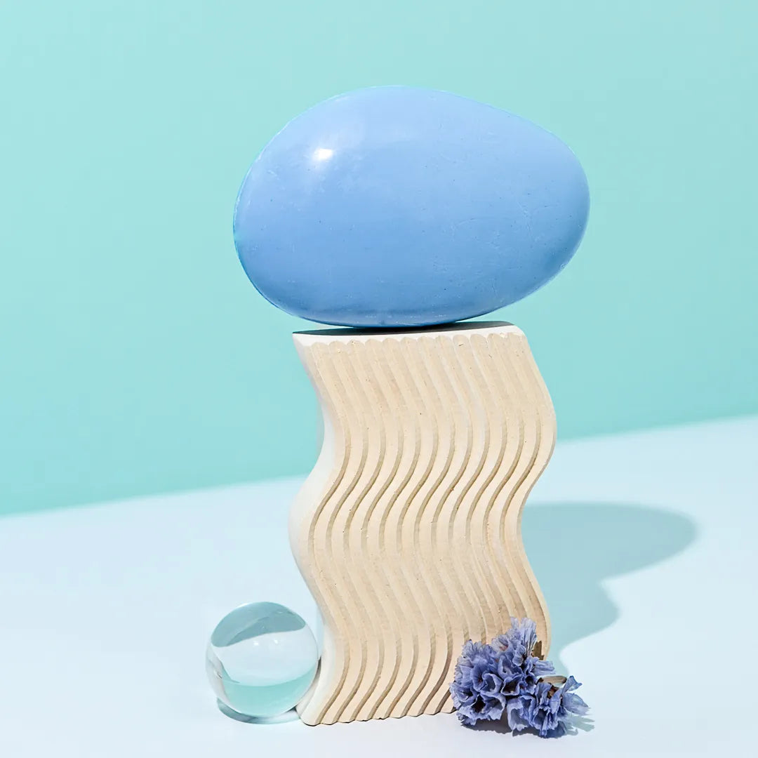 Savon bleu sur support ondulé, avec fleur mauve et boule transparente.